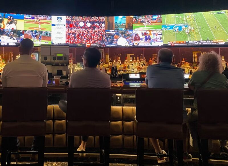 A group of people sitting at a bar watching TV